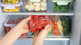 Woman taking plastic bag with frozen tomatoes from refrigerator, closeup