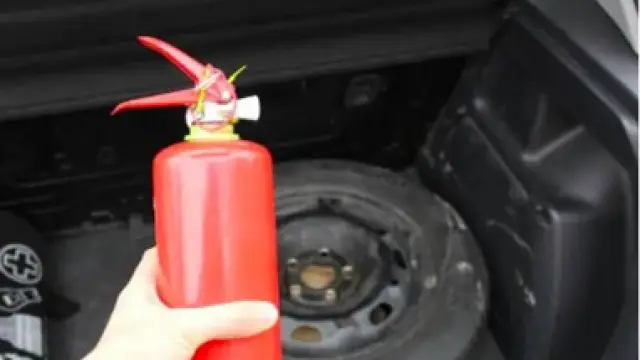 Un conductor sostiene un extintor antes de guardarlo en el maletero de su coche.