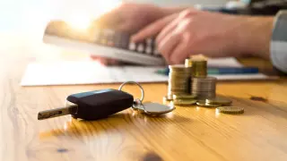 Un hombre con una calculadora, las llaves del coche y dinero en su mesa.